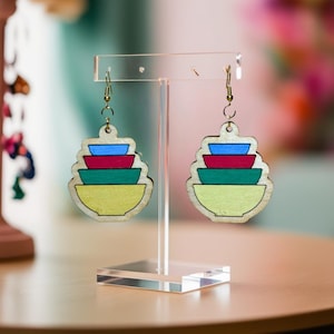May include: A pair of wooden earrings shaped like a stack of bowls. The bowls are painted in shades of yellow, green, red, and blue.
