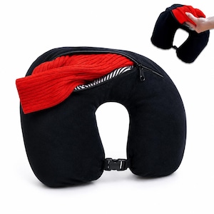 Può includere: Cuscino da viaggio nero a forma di U con uno scomparto con cerniera contenente un maglione rosso. Il cuscino ha una chiusura a fibbia. La cerniera è aperta, rivelando una fodera a righe.