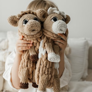 May include: Two handmade crochet sheep toys. The toys are mainly tan with brown and white details. They have large, dark eyes. The toys are being held by a person.