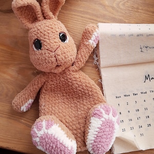 May include: A handmade, plush bunny in shades of tan, pink, and white. The bunny has large black eyes and is posed with one arm raised. The bunny is next to a calendar page showing the month of March.