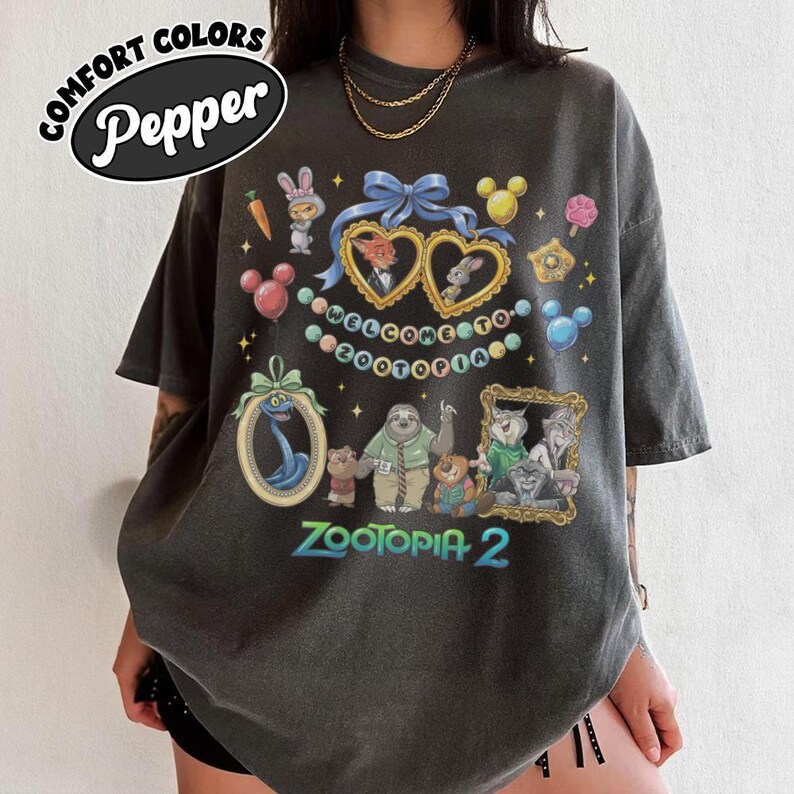 May include: Dark gray t-shirt with a colorful graphic featuring characters and the text "Welcome to Zootopia 2." The shirt has a distressed look and the words "Comfort Colors Pepper" in a circular design.