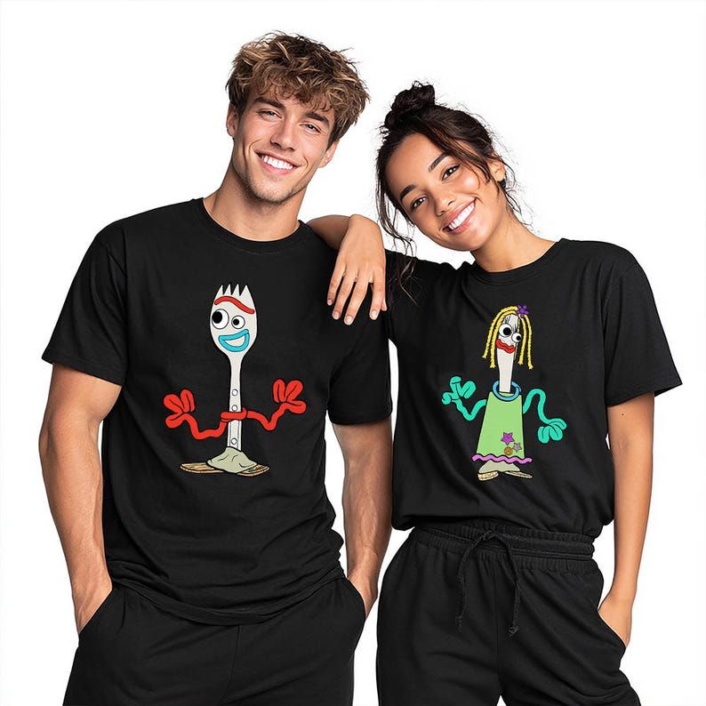 May include: Two black t-shirts featuring cartoon character graphics. The left shirt displays a white spork character with red pipe cleaner arms, googly eyes, and a blue mouth. The right shirt shows a spork character with yellow yarn hair, a green dress, and red lips.
