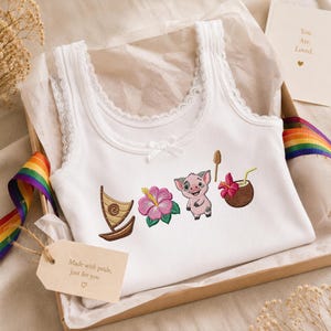 May include: A white ribbed tank top with lace trim at the neckline and a small white bow. The front features embroidered designs of a brown sailboat, a pink hibiscus flower, a small pig, and a coconut drink with a yellow straw.