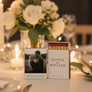 Peut inclure: Une boîte d'allumettes blanche avec le texte "OLIVIA and WILLIAM" et la date "15 - 04 - 26". La boîte est ouverte, révélant des allumettes à bout rouge. Une deuxième boîte présente une photo en noir et blanc d'un couple avec le texte "THE PERFECT MATCH".