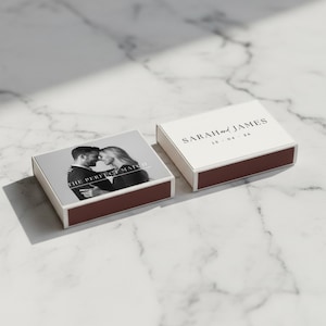 Puede incluir: Dos cajas de cerillas con exterior blanco y base rojo oscuro. Una caja presenta una foto en blanco y negro de una pareja con el texto "THE PERFECT MATCH". La otra caja tiene el texto "SARAH and JAMES" y la fecha "15.04.26".