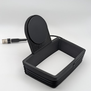 May include: A black matte charging stand featuring a rectangular frame base and a circular magnetic charging disc attached to an upright support. A black USB cable extends from the back of the unit, ending in a standard USB-A connector plug.