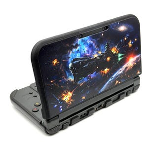 May include: Black handheld games console with a custom cover depicting a space battle. The cover shows a spaceship with a skull emblem, explosions, and a galaxy background. The console is open, showing the screen and buttons.