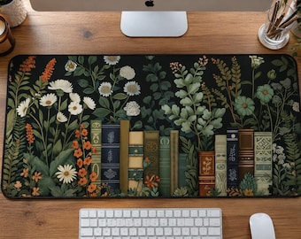 May include: A rectangular desk mat featuring a black background with a vibrant botanical illustration of various wildflowers, ferns, and foliage interspersed with a row of vintage-style book spines in shades of green, blue, brown, and cream.