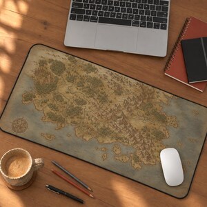 May include: A rectangular desk mat featuring a detailed fantasy map illustration with forests, mountain ranges, and a compass rose. The map has a vintage aesthetic with muted earth tones, tan landmasses, and blue water, finished with a black border.