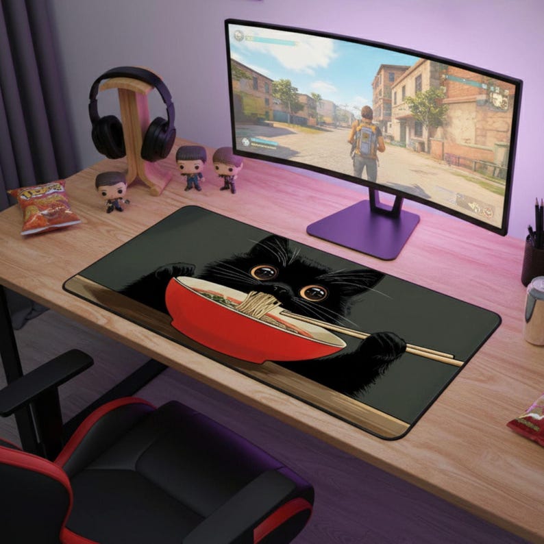 May include: A black rectangular mousepad featuring a cartoon black cat eating ramen from a red bowl with chopsticks. The mousepad is on a wooden desk with a computer monitor, headphones, and figurines.