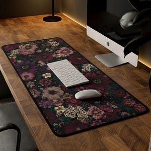 May include: A rectangular floral mouse pad featuring a dark background with burgundy, purple, and cream-colored flowers. A white keyboard and mouse are on the pad, which sits on a wooden desk.