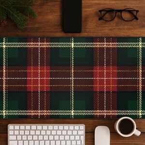 May include: A green, red, and white plaid desk mat. The mat is rectangular and features a classic tartan pattern. A keyboard, mouse, coffee cup, glasses, and a smartphone are on the wooden desk.