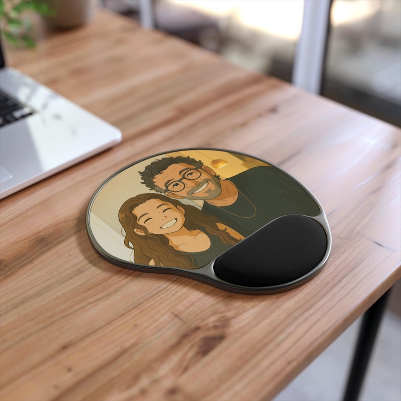 Pode incluir: Tapete de rato ergon&oacute;mico com apoio para o pulso. O tapete apresenta uma ilustra&ccedil;&atilde;o de desenho animado de um casal sorrindo. O tapete tem um apoio para o pulso preto e uma moldura prateada. O tapete do rato est&aacute; numa secret&aacute;ria de madeira.