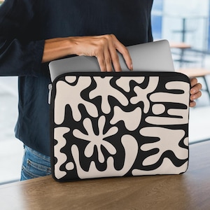 Puede incluir: Una funda para portátil negra y blanca con un patrón abstracto de formas beige. La funda está hecha de un material suave y duradero y está diseñada para proteger tu portátil de arañazos y golpes.