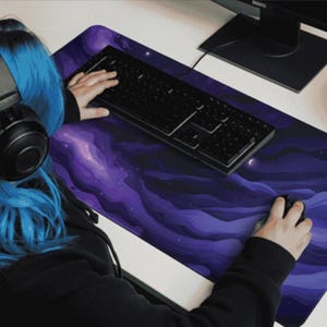 May include: A large rectangular purple and blue mousepad with a nebula design. A black keyboard and mouse are on the pad. The mousepad has a crescent moon and stars design.
