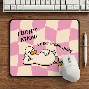 May include: Pink and white checkered mousepad with a pixelated duck illustration. Text reads "I DON'T KNOW I JUST WORK HERE". A white mouse and pen are also visible.