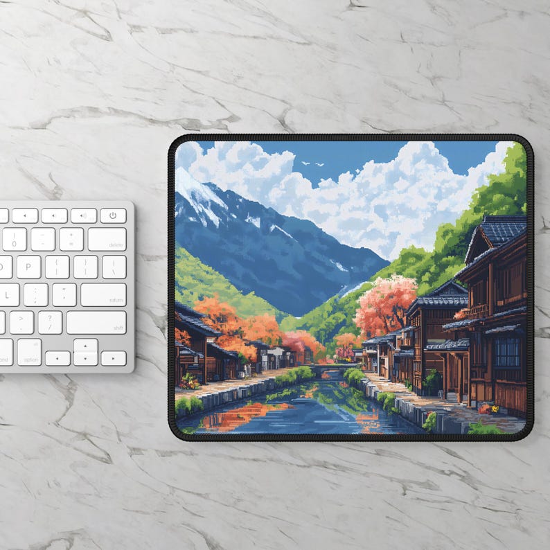 May include: A rectangular mousepad featuring a serene landscape painting. The artwork depicts a river flowing through a village with traditional wooden buildings, surrounded by mountains and colorful autumn trees. A white keyboard is visible on the left.
