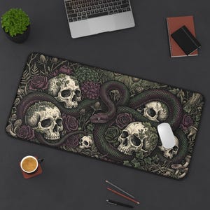 May include: A rectangular desk mat featuring a dark, detailed illustration of multiple human skulls intertwined with a long, winding snake. The design is accented with deep purple roses, green foliage, and various botanical elements on a black background.