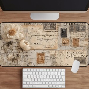 May include: A rectangular mouse pad with a vintage design featuring cream-colored flowers, postage stamps, and handwritten script. The pad is placed on a wooden surface with a white keyboard and mouse.
