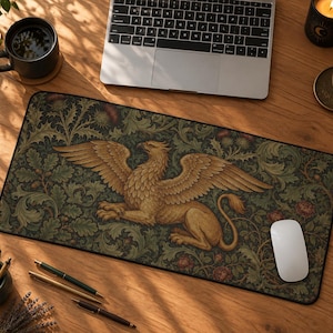 Puede incluir: Una alfombrilla de escritorio rectangular con una ilustración central de un grifo dorado rodeado de un intrincado follaje verde oscuro, hojas de roble y pequeños detalles florales rojos. La alfombrilla tiene un borde negro y superficie lisa.