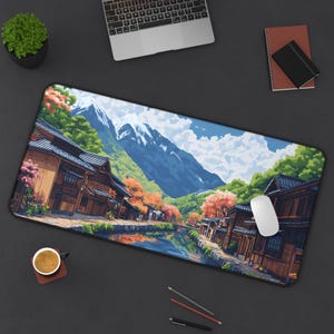 Pixel art desk mat of a traditional Japanese village with wooden buildings, a canal, cherry blossom trees, and snow-capped mountains in the background. The scene is colorful, with reflections in the water, a blue sky, and green hills.