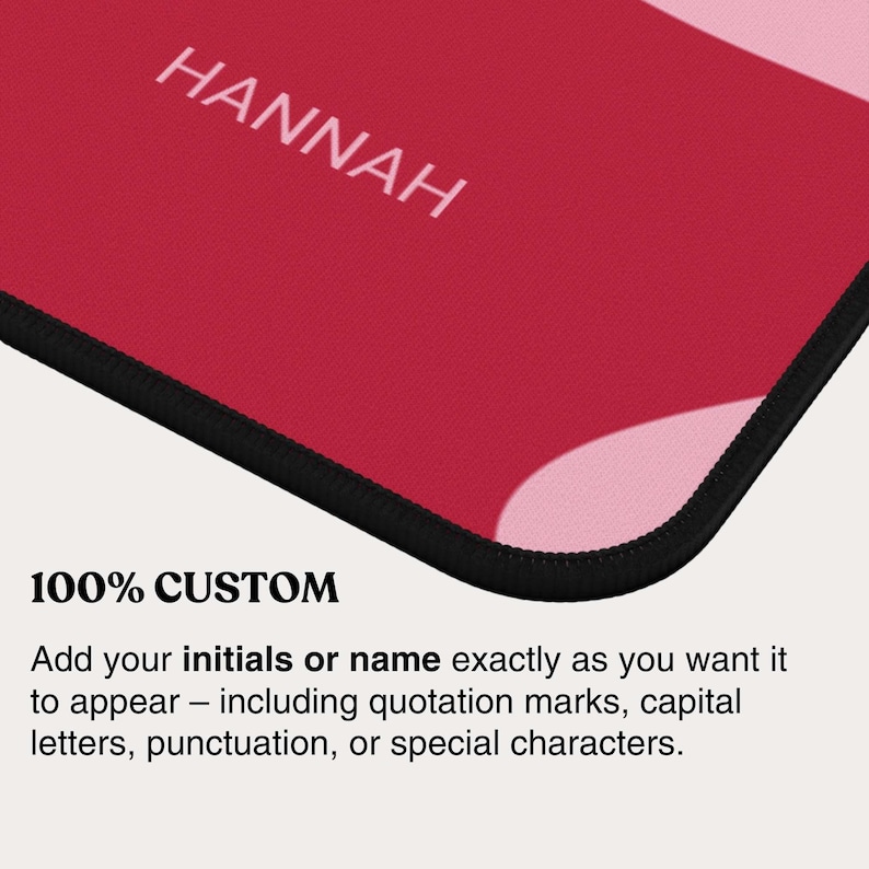 May include: A rectangular mouse pad featuring a vibrant red and light pink abstract pattern with the name HANNAH printed in white capital letters. The mouse pad has a black stitched edge and includes text stating 100% CUSTOM and instructions.