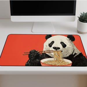 May include: A rectangular red mouse mat featuring a panda eating noodles with chopsticks. The panda is black and white, and the noodles are yellow. The mat has a black border and is designed for computer use.