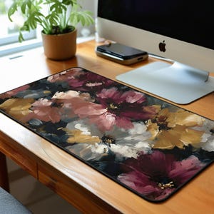 May include: A rectangular mouse pad featuring a floral design. The artwork showcases large, abstract flowers in shades of burgundy, pink, white, and gold against a dark background. The mouse pad is placed on a wooden desk.