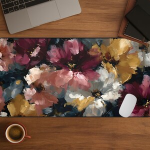 May include: A floral mousepad featuring a vibrant, painterly design of large flowers in shades of pink, white, yellow, and burgundy against a dark background. A white computer mouse is on the right side of the mousepad. A laptop and a cup of coffee are also visible.