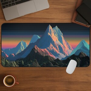 May include: A rectangular mousepad featuring a vibrant mountain range design. The mountains are rendered in shades of blue, pink, and orange, set against a striped sunset sky. The mousepad is on a wooden desk, with a laptop, coffee cup, and mouse.