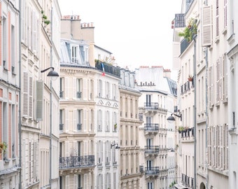 May include: A narrow street in Paris, France, lined with white buildings with windows and balconies. The buildings have a classic Parisian architecture with shutters and ornate details.
