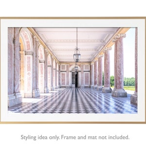 May include: A framed print of a classical colonnade with pink marble columns and arched openings. The black and white checkered floor leads to a distant doorway. Two ornate hanging lanterns illuminate the space. The frame is gold.
