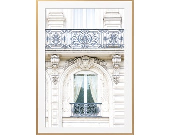 May include: A white building with a large arched window and a balcony with a black wrought iron railing. The balcony is on the second floor of the building. The window is framed by ornate white trim.