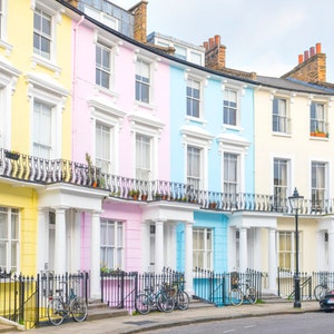 May include: A row of colorful Victorian townhouses with white trim and black railings. The houses are painted in shades of yellow, pink, blue, and light blue. There are bicycles parked in front of the houses and a car parked on the street.