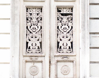 Puede incluir: Una puerta doble blanca con intrincados detalles tallados y un acabado desgastado. La puerta está enmarcada por un marco blanco y se encuentra contra una pared blanca.