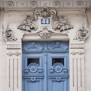 May include: A blue double door with ornate carvings and a white number "44" above it. The door is set in a white stone building with decorative details.
