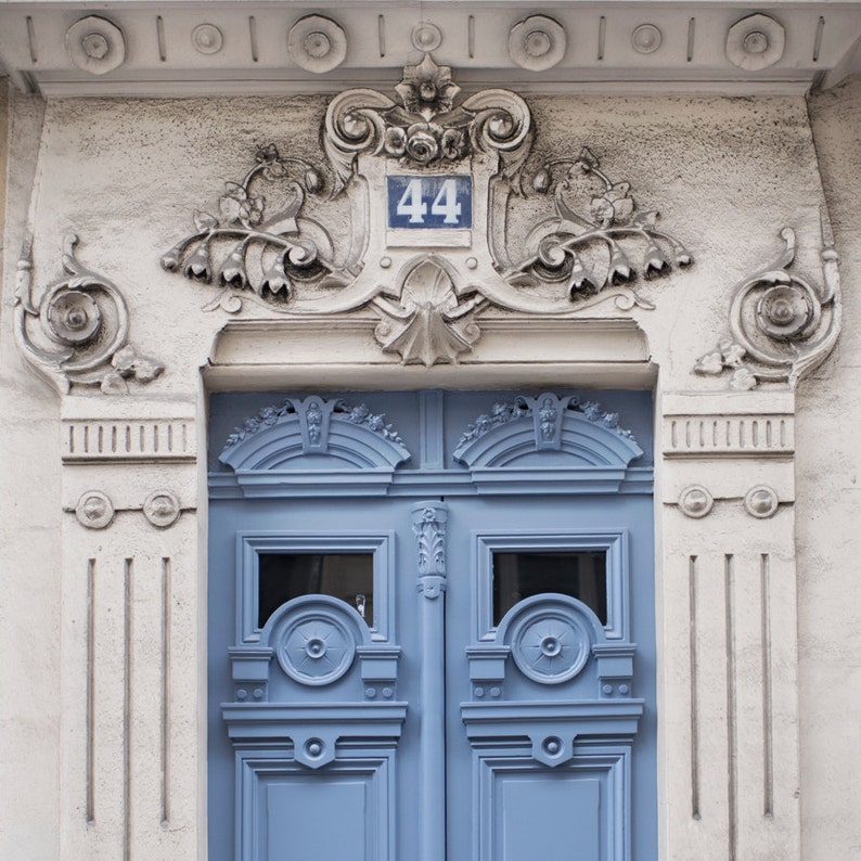 May include: A blue double door with ornate carvings and a white number "44" above it. The door is set in a white stone building with decorative details.