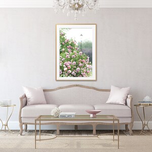 May include: A living room with a light pink sofa, gold side tables, and a framed picture of pink flowers. The room has a neutral colour palette with a rug and a chandelier.