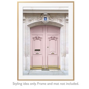 May include: A vintage pink double door with gold accents and a blue number "2" above the door. The door is set in a white stone building with ornate details.
