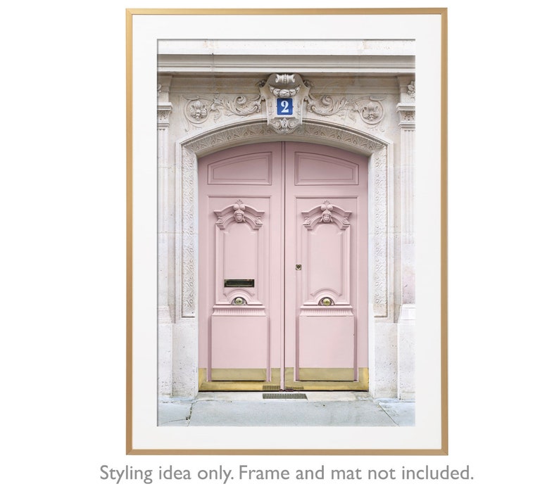 May include: A vintage pink double door with gold accents and a blue number "2" above the door. The door is set in a white stone building with ornate details.