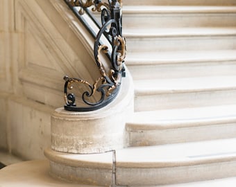 May include: A white marble staircase with a black wrought iron railing with gold accents. The railing has a decorative design with scrolls and leaves.