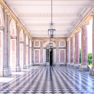 May include: An interior shot of a colonnade with pink marble columns and a checkered floor. The ceiling is white with ornate molding, and two hanging lanterns illuminate the space. A doorway is visible at the end.
