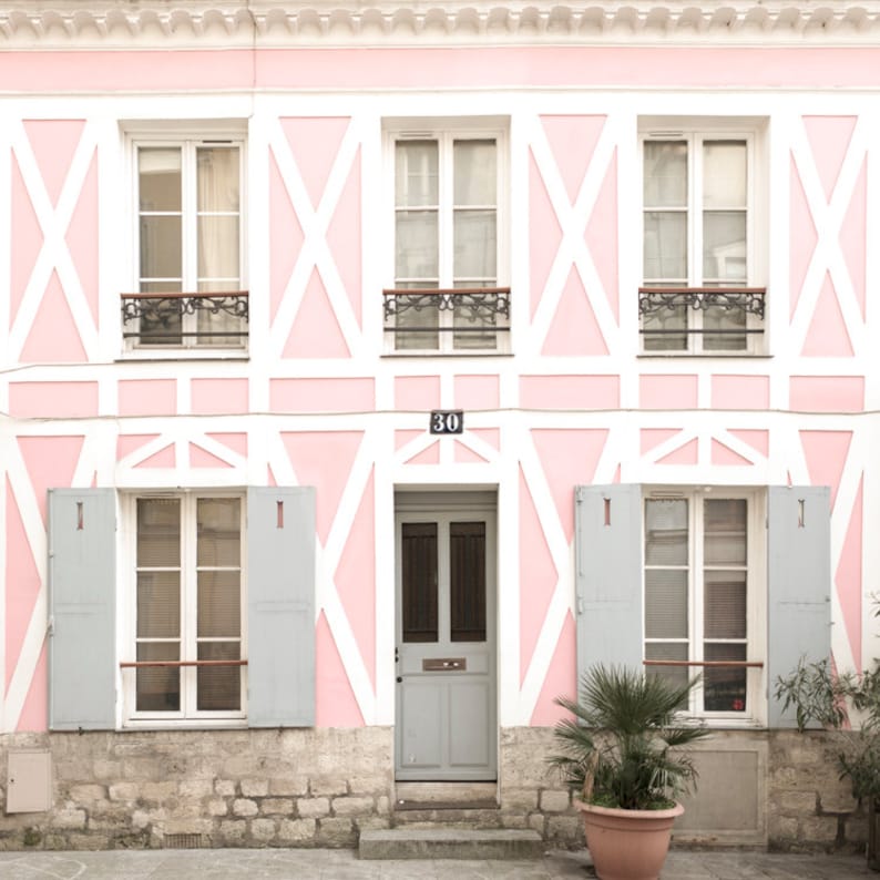 May include: A pink building with white trim and a gray door. The building has three windows on each floor, and the windows are all white with black trim. The door has a number "30" above it.