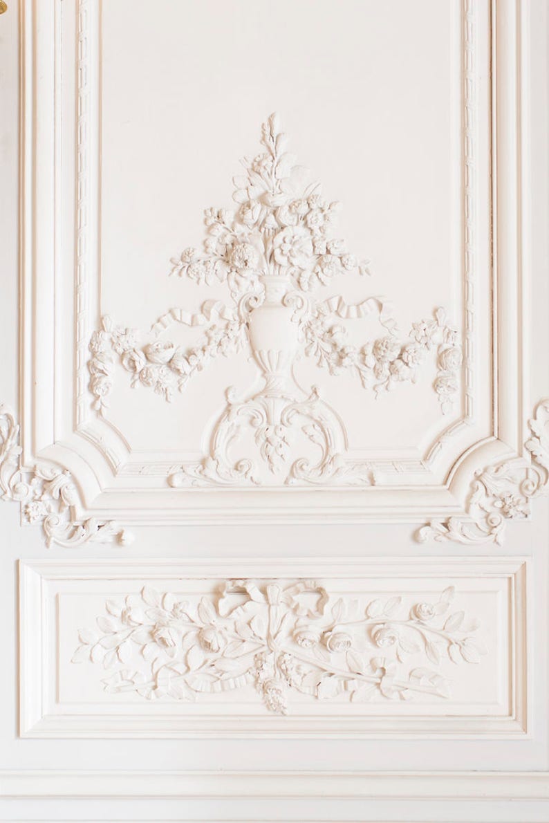 May include: White plaster molding with intricate floral designs and a vase in the center. The molding is on a white wall.