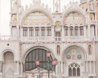 May include: A view of a large, ornate building with a series of arches and windows. The building is made of white stone and has a light pink hue. There are several street lamps in the foreground, with pink lampshades.