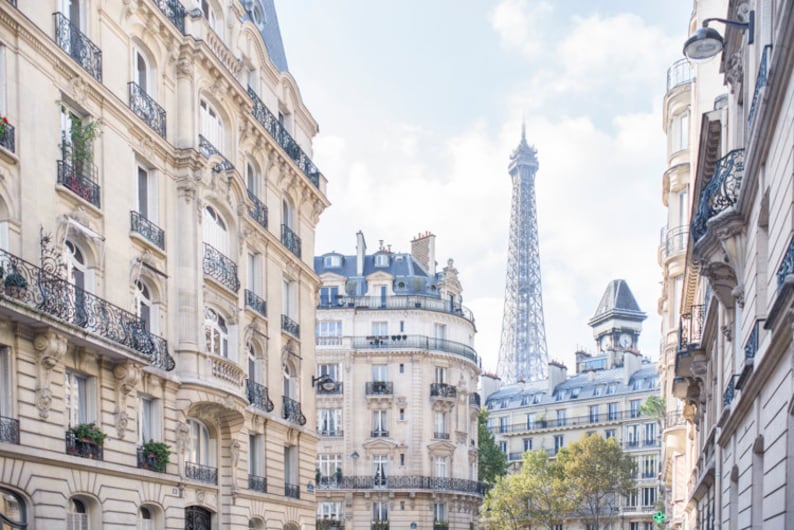 May include: A view down a narrow street in Paris, France, with the Eiffel Tower in the distance. The street is lined with tall, white buildings with balconies.