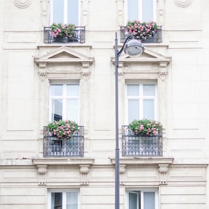 May include: A white building with four windows and balconies. Each balcony has a wrought iron railing and is decorated with pink flowers.