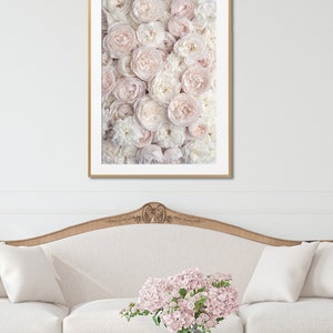 Pu&ograve; includere: Una stampa incorniciata di un muro di rose rosa e bianche. La stampa &egrave; appesa sopra un divano bianco con un tavolino da caff&egrave; in vetro e un vaso di fiori rosa.