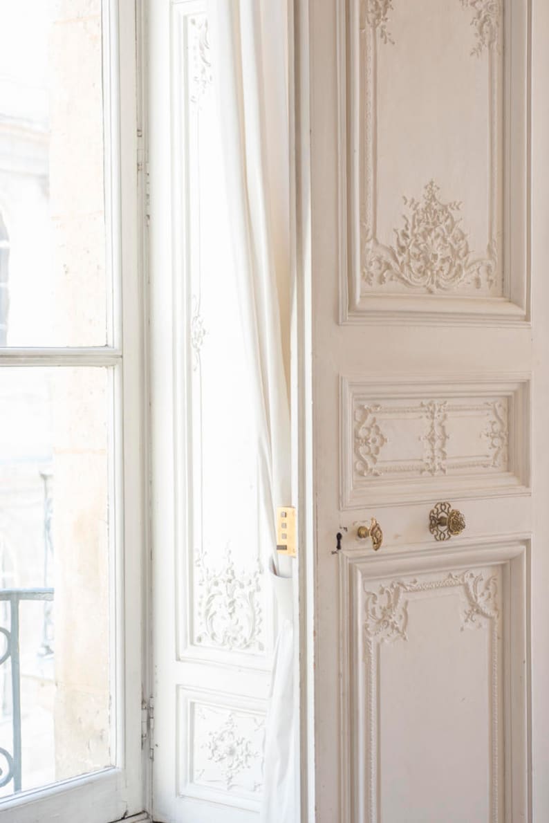 May include: A white door with intricate carvings and gold hardware. The door is open and a white curtain is partially visible behind it.