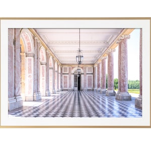 May include: A framed print of a classical colonnade with pink marble columns and a black and white checkered floor. Two ornate hanging lanterns illuminate the corridor. The print is set in a gold frame.
